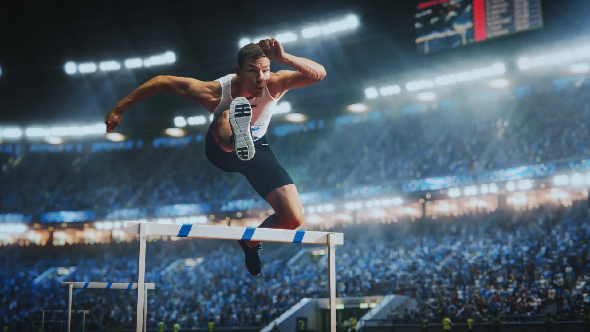 Athlete clearing a hurdle in a floodlit stadium